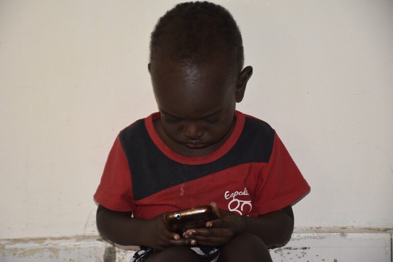 A child looks closely at a smartphone screen.